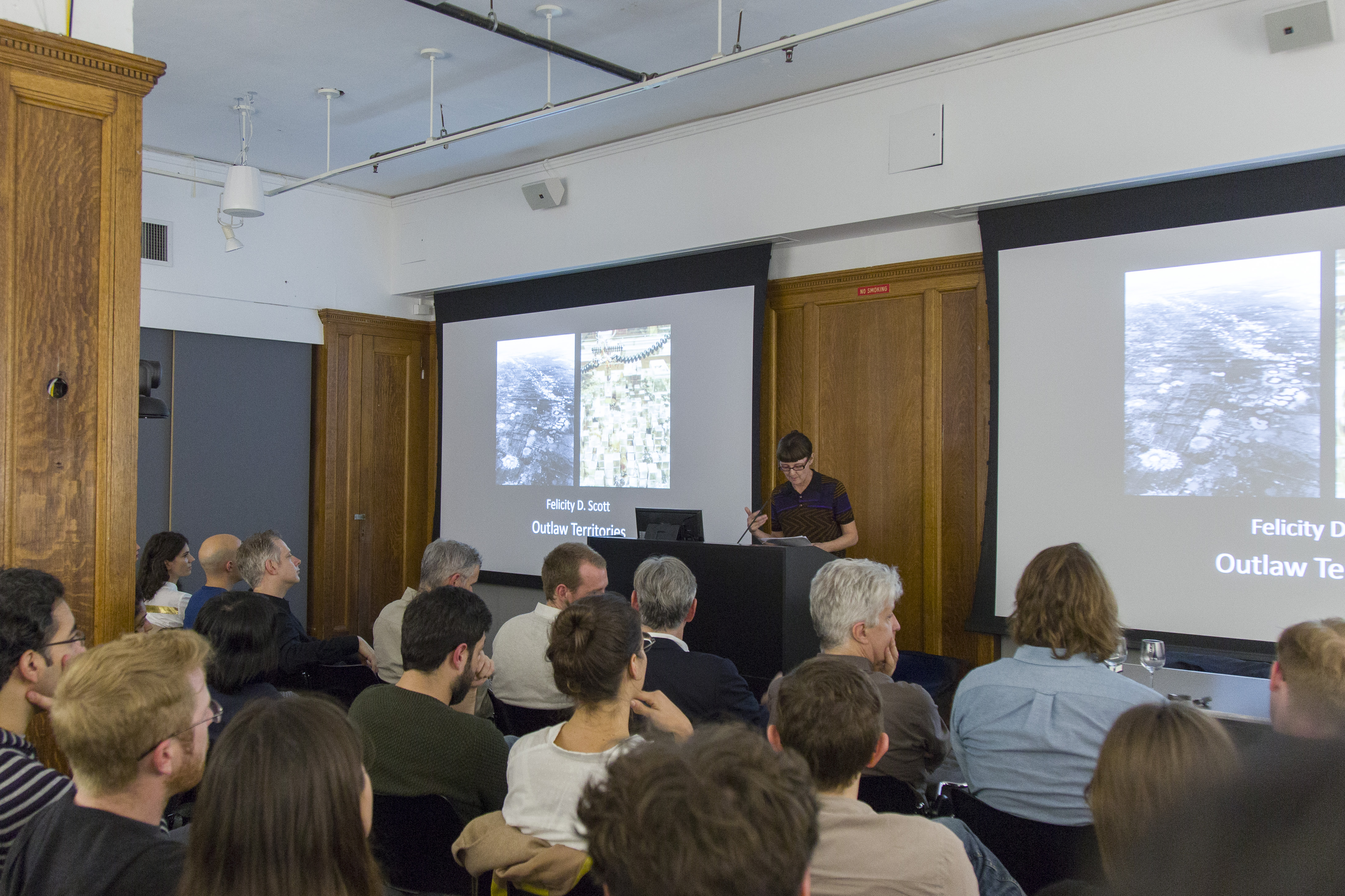 A woman at a podium speaking to a group of people seated in front of her
