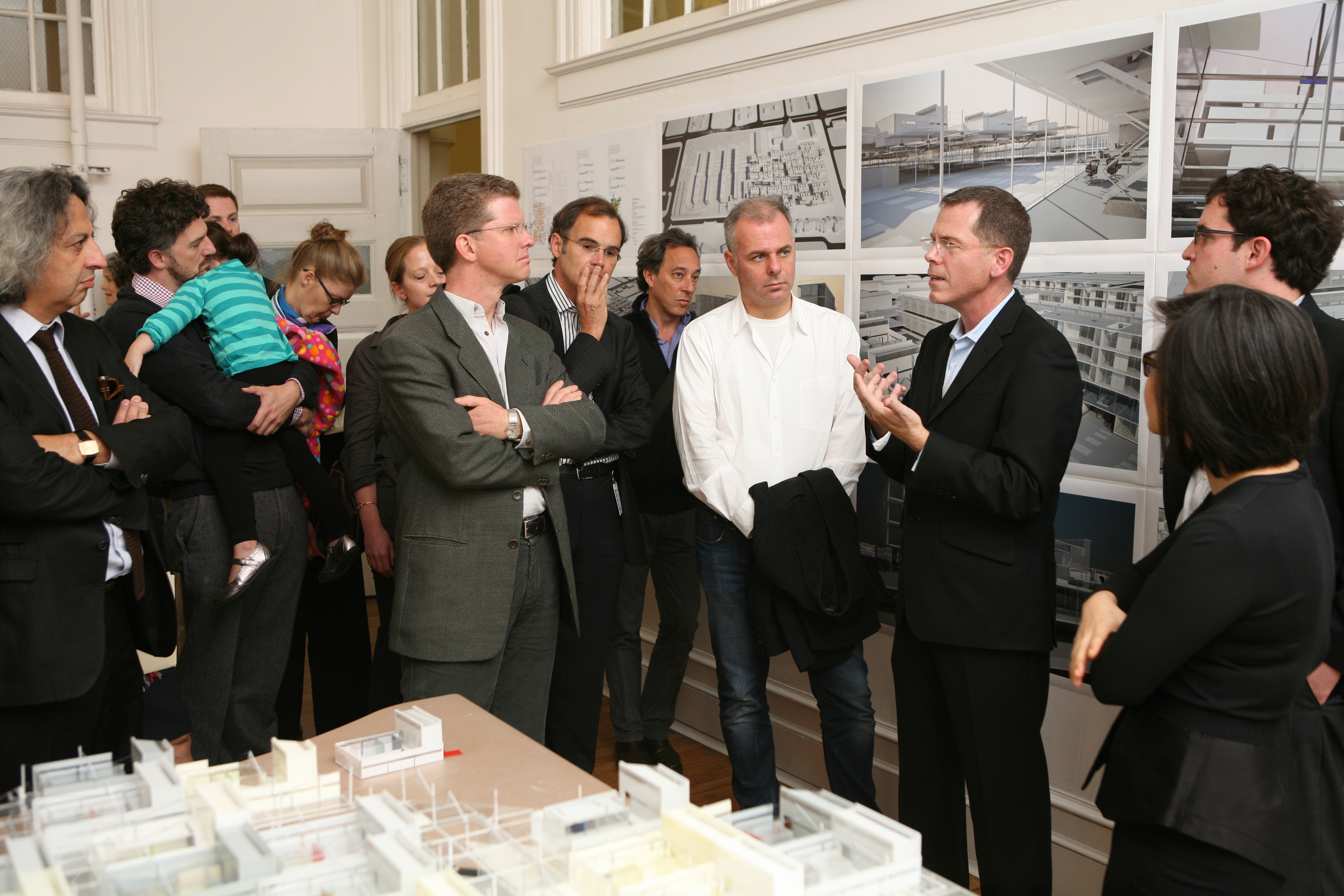 A man speaking to a group of people in front of a wall