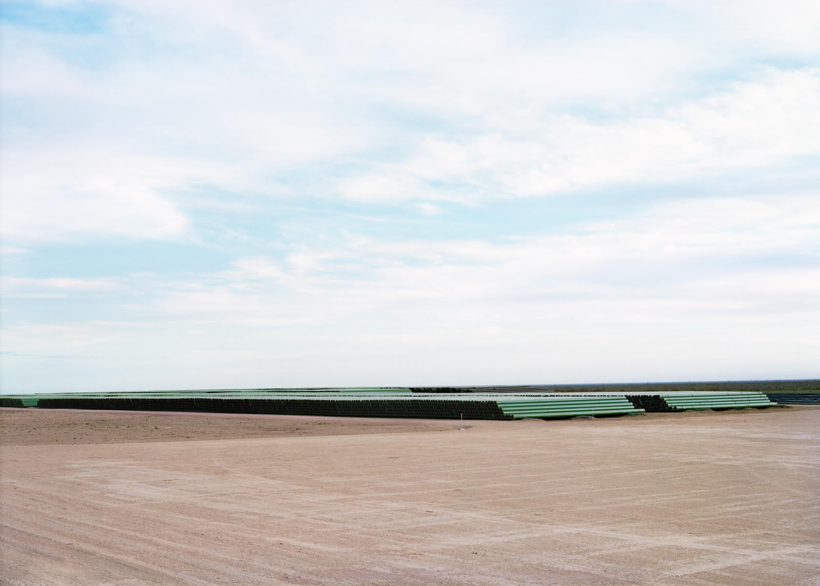 A photograph of a dry landscape and blue sky with clouds; in the distance are stacks of green pipes