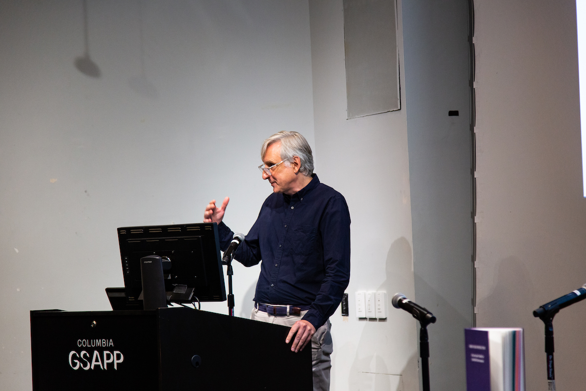 Reinhold Martin stands at a podium introducing the book