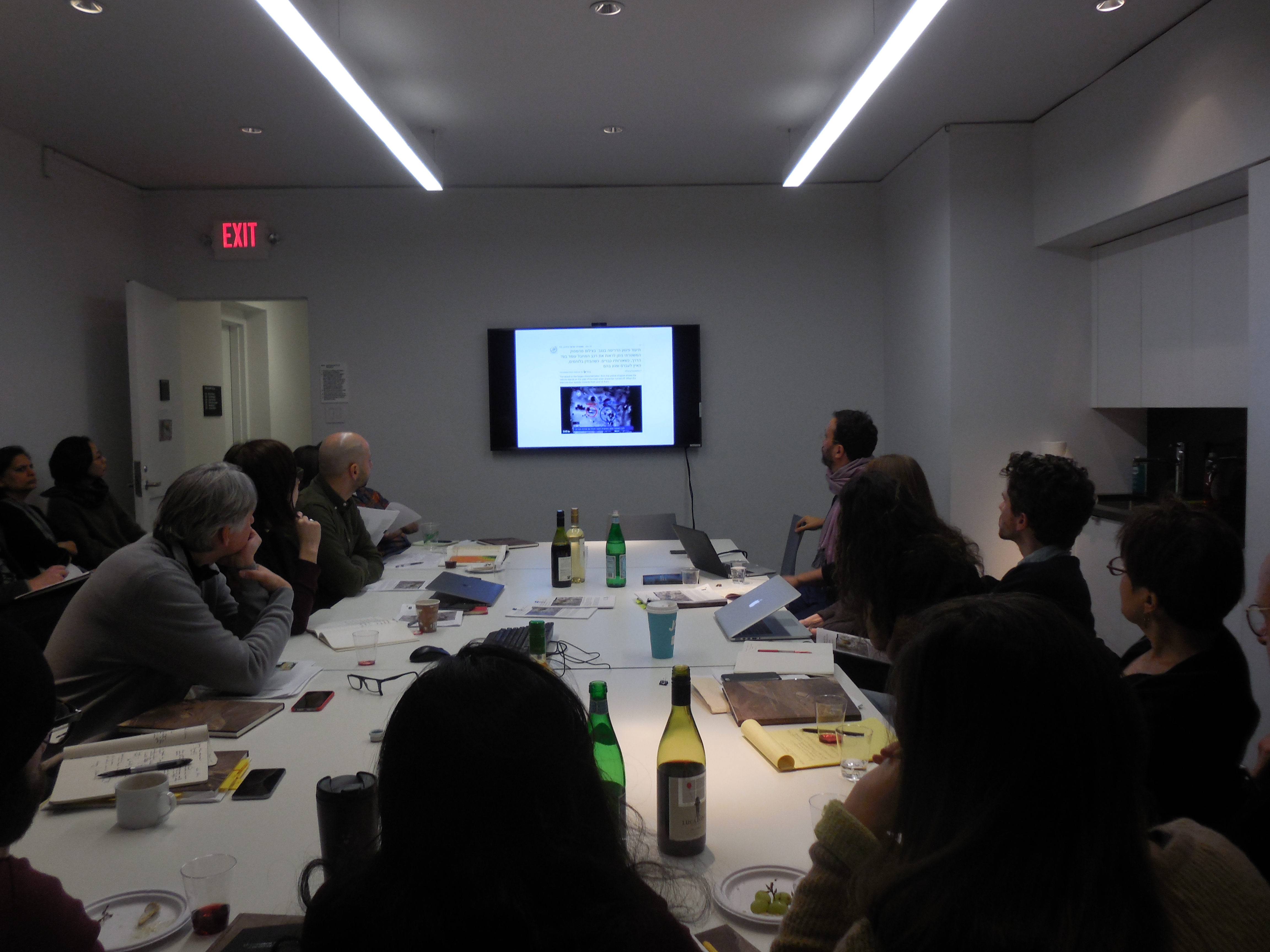 A group gathered around a conference table looking at a screen with a presentation