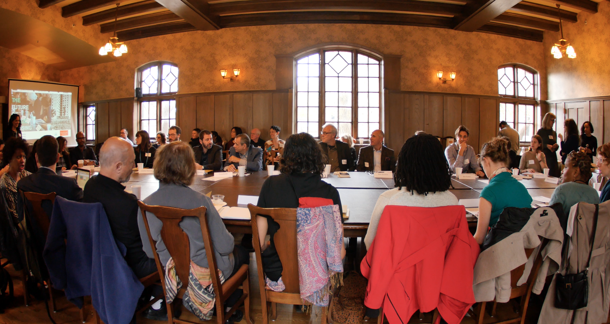 Wide angled photograph of the long table where people are gathered for the conference