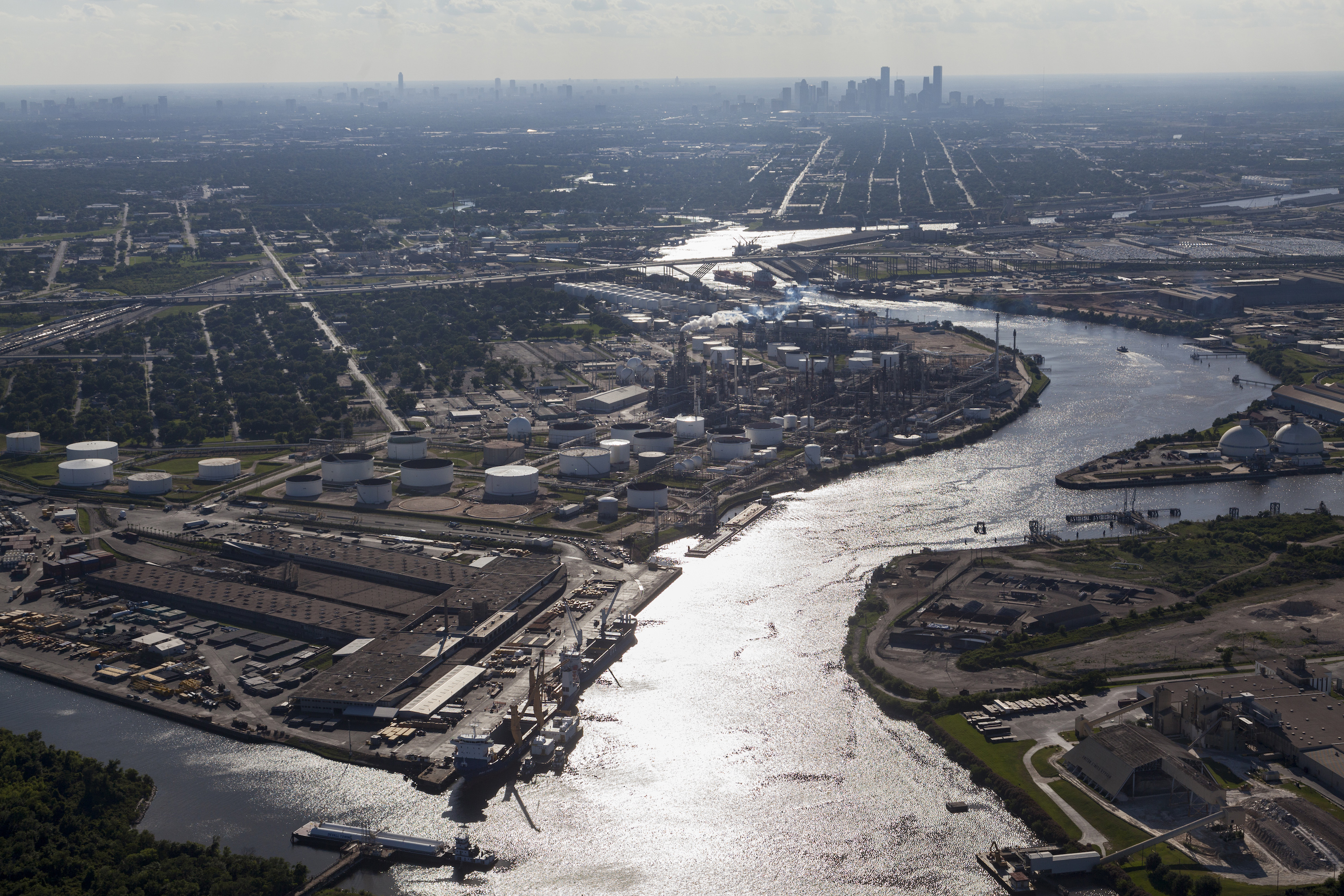 An aerial view shows a curving water source with infrastructure on either side, and a city in the distance