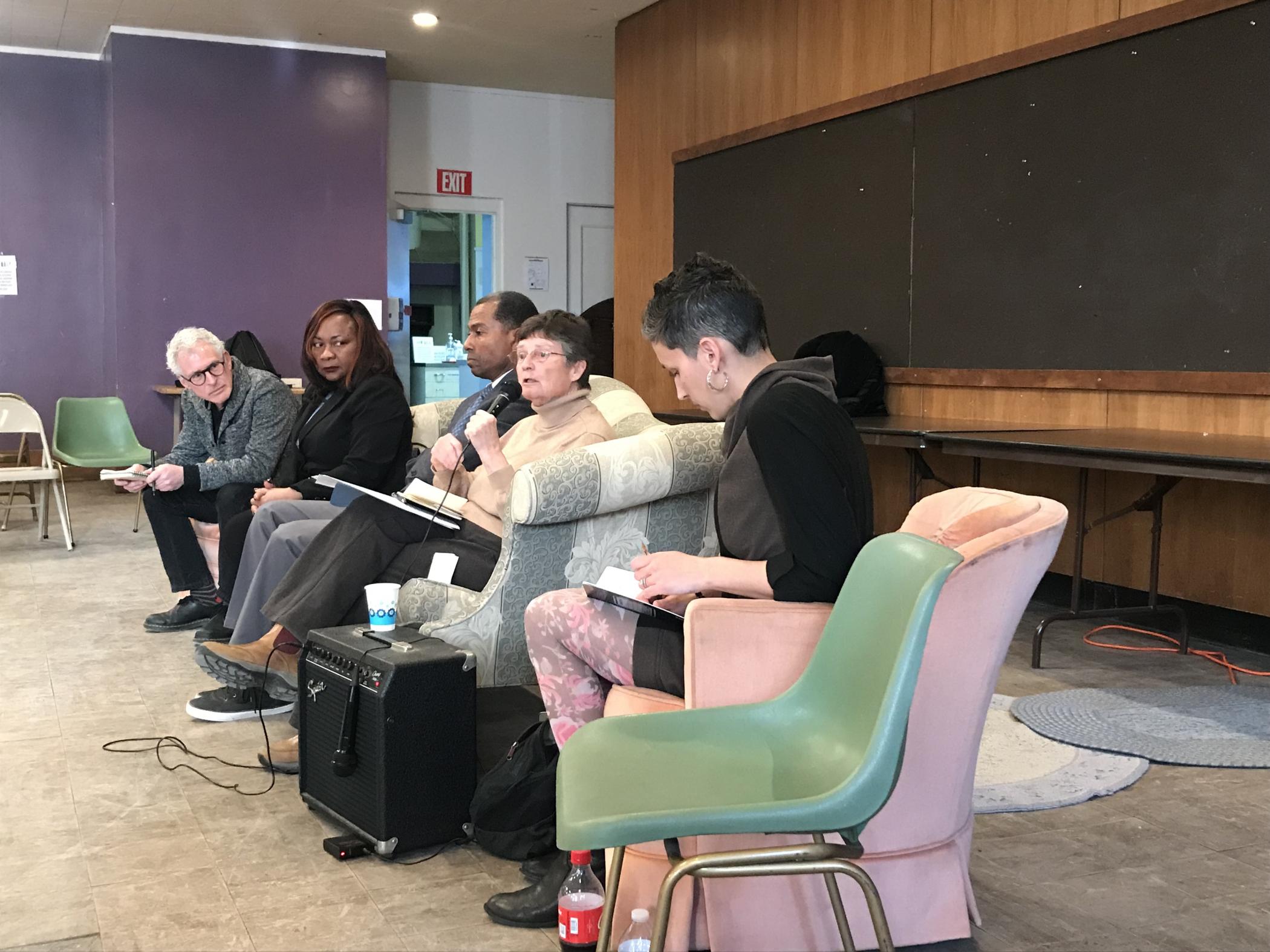 The panelists seated at the front of the room on a couch.