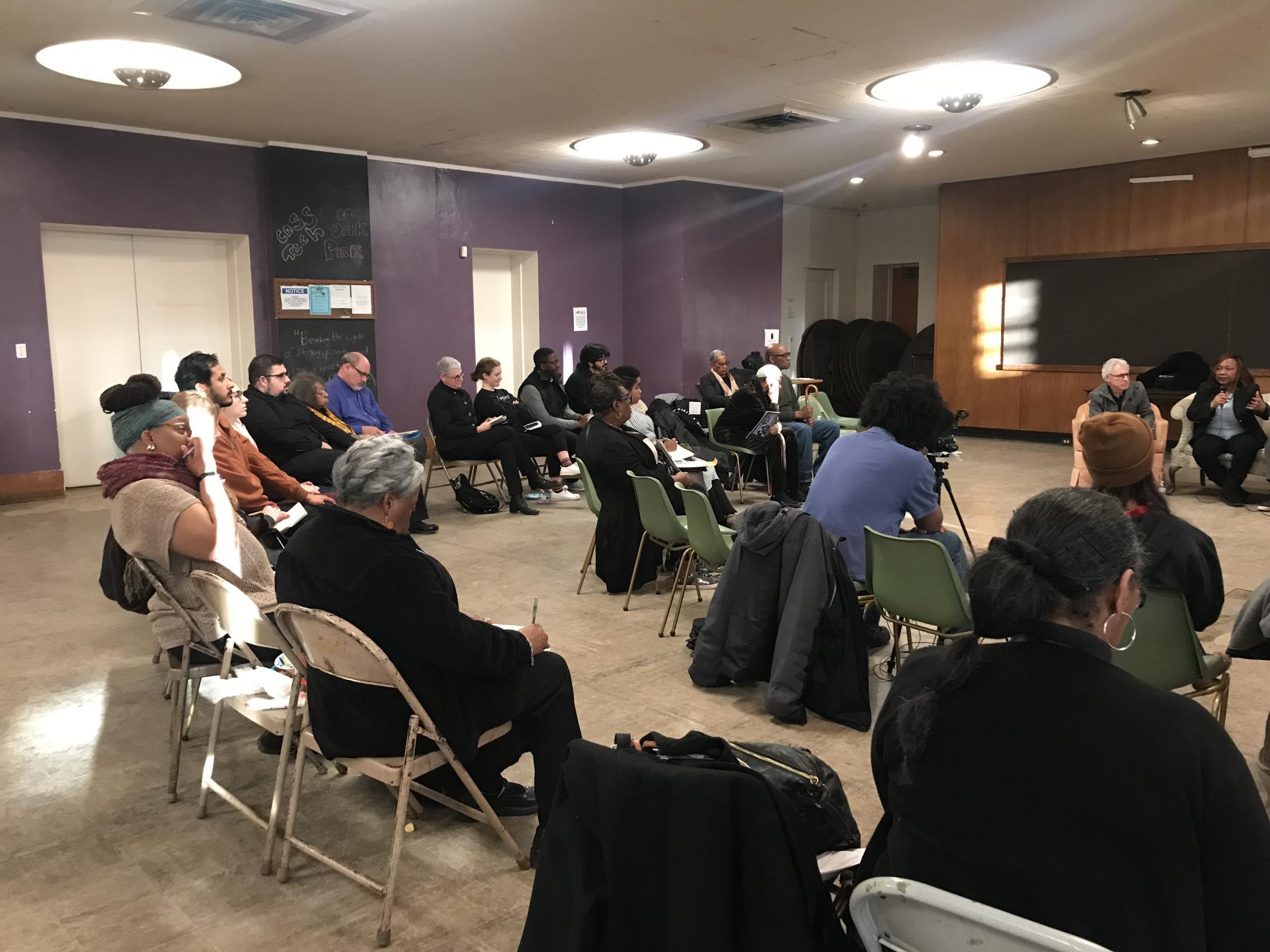 A room filled with people seated in a semi-circle configuration