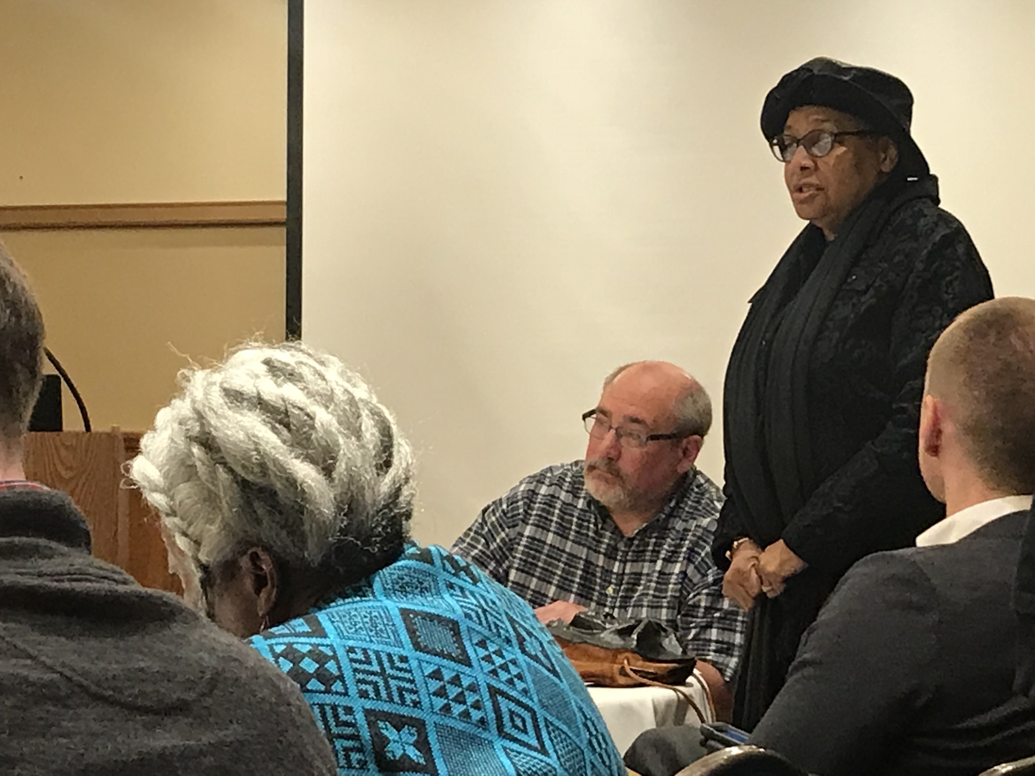Someone standing up to speak in front of a long table.