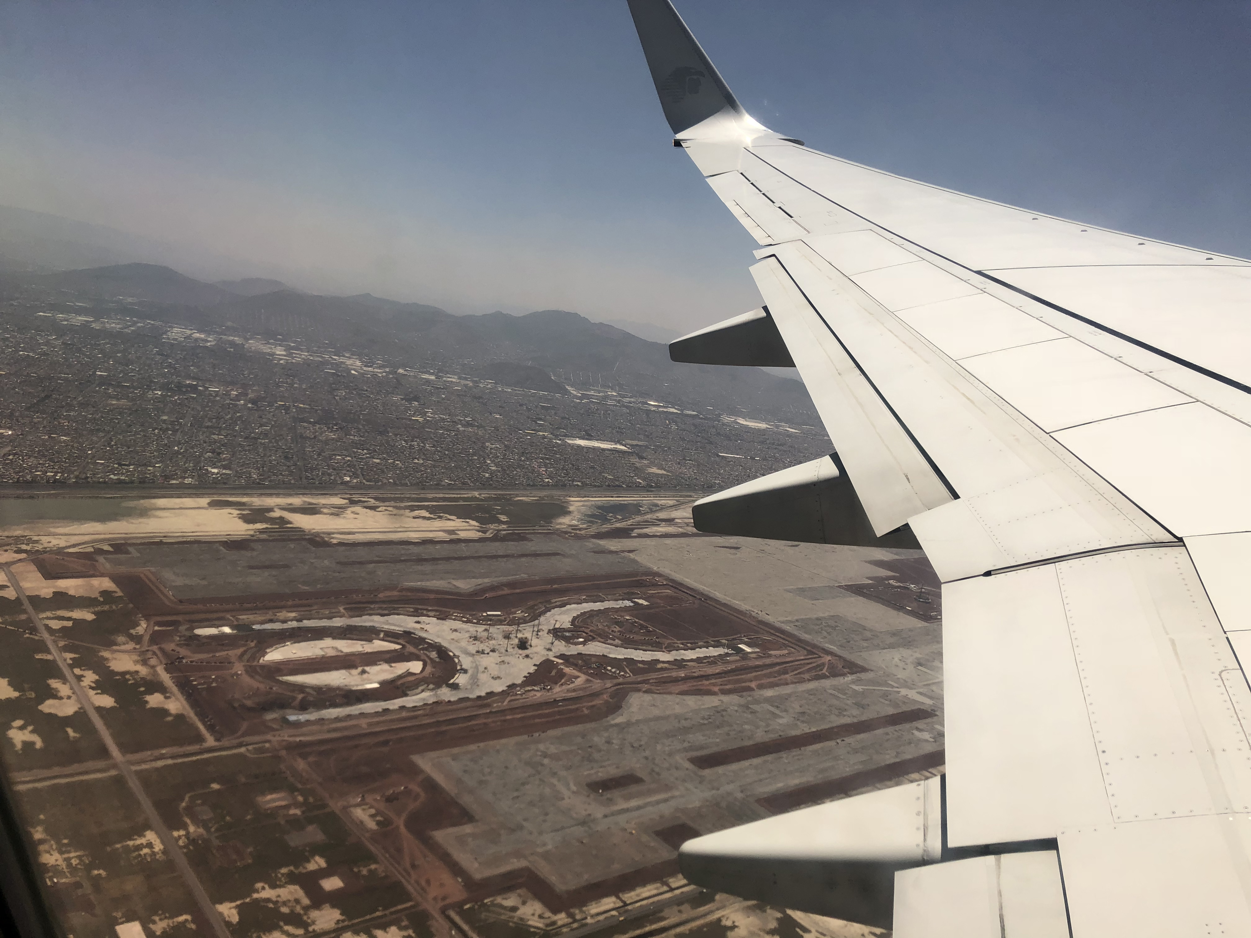 A photograph from an airplane showing part of a plane wing and land below